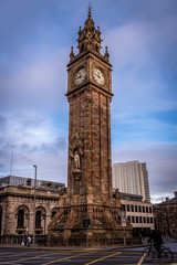 Fototapeta premium BELFAST, NORTHERN IRELAND, DECEMBER 19, 2018: People passing by Queen's Square where Albert Memorial Clock Tower is situated. Completed in 1869 and is one of the best known landmarks of Belfast.