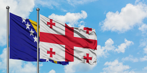 Bosnia Herzegovina and Georgia flag waving in the wind against white cloudy blue sky together....