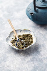 Dried Green Tea Leaves and Iron Tea Pot on bright wooden Background. Close up. Copy space. 