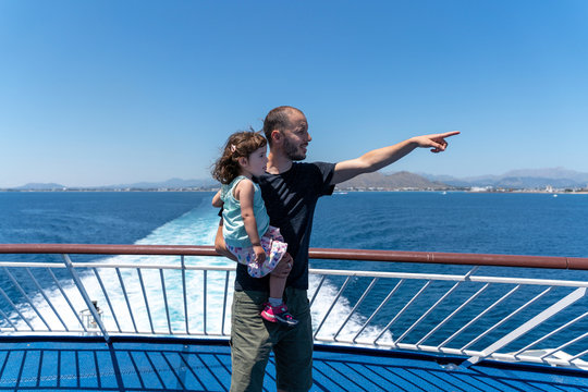 Father standing on the deck of a ship with little daughter on his arm pointing at distance, Mallorca, Spain