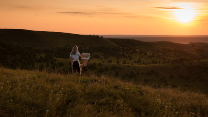 The artist paints a picture outdoors in the early sunny morning. Painting in nature.	