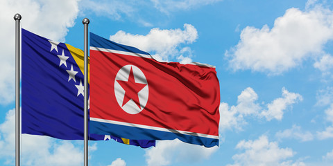 Bosnia Herzegovina and North Korea flag waving in the wind against white cloudy blue sky together....