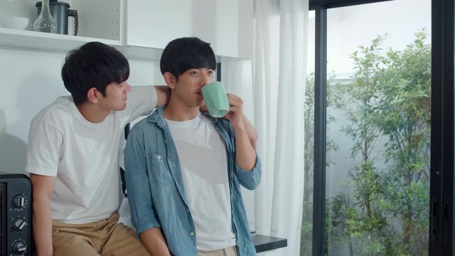Asian gay couple drinking coffee, having a great time at home. Young handsome LGBTQ+ men talking happy relax rest together spend romantic time in modern kitchen at house in the morning concept.