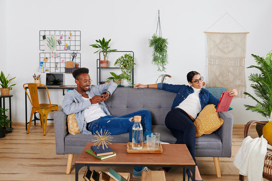 Multiethnic couple spending time together at living room, woman using tablet and man smartphone