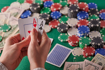 A player in a poker casino holds a pair of aces against the background of chips and money of dollars. Victory, success. Gaming business.