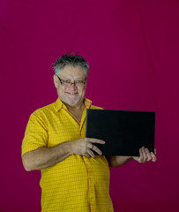 An elderly man with gray hair holds a laptop in his hands. Different emotions are expressed on the face. Joy, pleasure, obscurity, thoughtfulness, delight, tenderness. Portrait of a man in a yellow sh