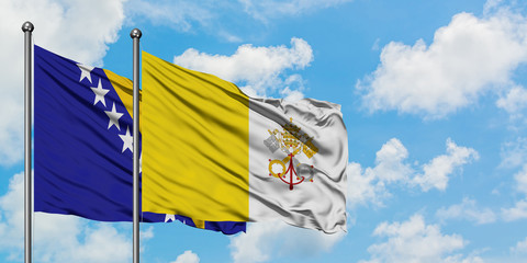 Bosnia Herzegovina and Vatican City flag waving in the wind against white cloudy blue sky together. Diplomacy concept, international relations.
