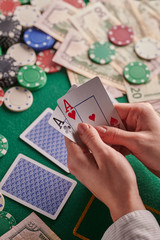 A player in a poker casino holds a pair of aces against the background of chips and money of dollars. Victory, success. Gaming business. Vertical shot.