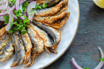 Fried anchovies fish and purple onion on the plate.