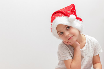 Llittle boy in Santa Claus hat looking at camera, holds his chin up on white background. Postcard. Waiting for Xmas, Happy new year. Copy space