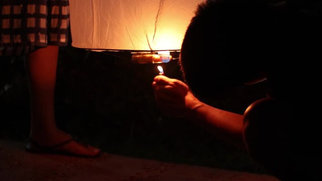 4k Asian Young man light up the Floating lanterns while prepare for launching to sky in Yee Peng Festival, Loy Krathong traditional festival in Chiangmai, Thailand, night time, family activitiy, warm