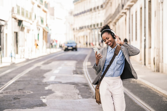 Happy young woman with headphones and mobile phone in the city on the go, Lissabon, Portugal
