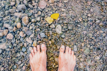 Bare feet cooling off in a stream full of pebbles, revitalizing massage in nature.