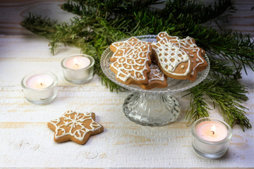Gingerbread Christmas cookies on a festive glass bowl with burning candles and fir branch decoration on a white painted wooden table, copy space, selected focus