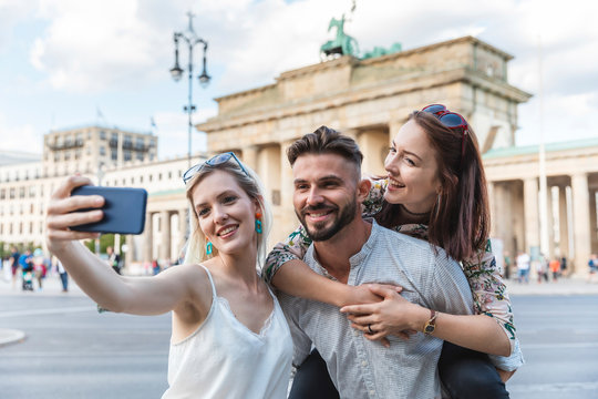 Portrait of three friends taking selfie with cell phone in front of Brandenburger Tor, Berlin, Germany