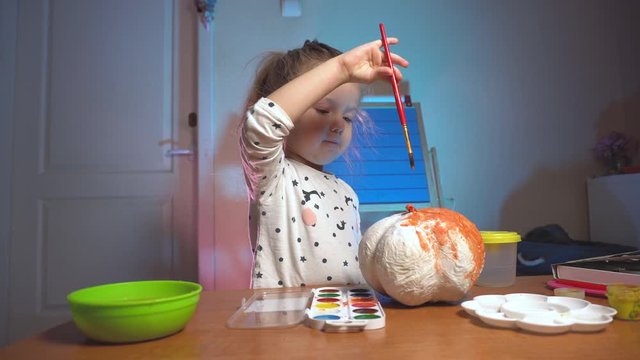 Little girl colorizing fake craft pumpking in orange color
