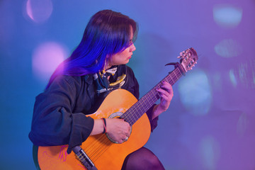 Fototapeta na wymiar Latin woman playing an acoustic guitar on purple background with drained blue and light sparkles