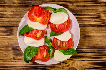 Plate with caprese salad (italian salad with cherry tomatoes, mozzarella cheese and basil leaves) on wooden table. Top view