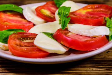 Plate with caprese salad (italian salad with cherry tomatoes, mozzarella cheese and basil leaves) on wooden table