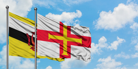 Brunei and Guernsey flag waving in the wind against white cloudy blue sky together. Diplomacy concept, international relations.