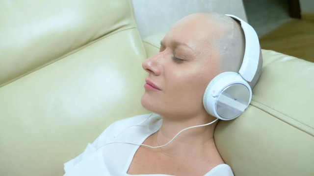 close-up. a bald woman in headphones listens to music and moves her head to the beat of the music.