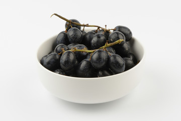 Racimo de uvas negras en un bol de cerámica blanco