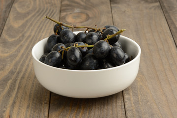 Racimo de uvas negras en un bol de cerámica blanca en la mesa