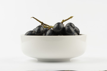 Racimo de uvas negras en un bol de cerámica blanco