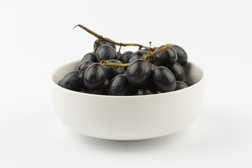 Racimo de uvas negras en un bol de cerámica blanco