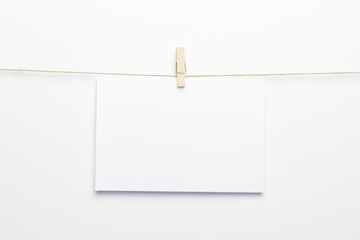 Pinza colgando de una cuerda con una tarjeta en blanco sobre fondo blanco - obrazy, fototapety, plakaty