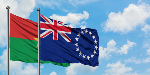 Burkina Faso and Cook Islands flag waving in the wind against white cloudy blue sky together....