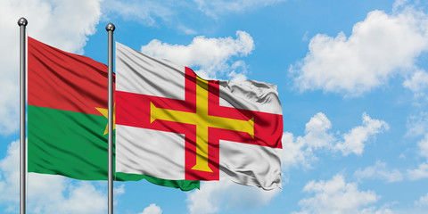 Burkina Faso and Guernsey flag waving in the wind against white cloudy blue sky together. Diplomacy concept, international relations.