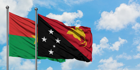 Burkina Faso and Papua New Guinea flag waving in the wind against white cloudy blue sky together. Diplomacy concept, international relations.
