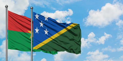 Burkina Faso and Solomon Islands flag waving in the wind against white cloudy blue sky together. Diplomacy concept, international relations.