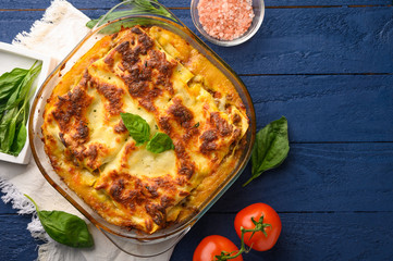 Italian lasagna, on a blue wooden background. Culinary background, Italian recipe book, delicious food. With space for design, top view.