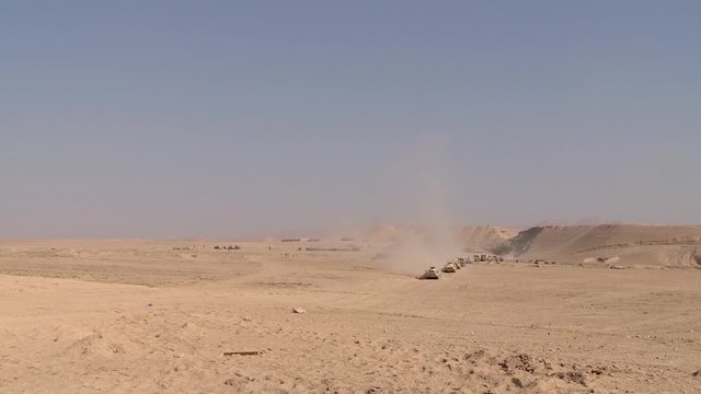 A military convoy of heavy vehicles rides through the desert, the dust rises. Zone of military conflict.