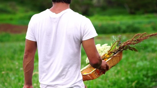 Young gardener florist man walking with flowers bouquet in countryside farm. Concept of organic gardening, sustainable agriculture, ecology, connection to nature, healthy lifestyle hobby. Slow motion.