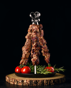Tower of shish kebab skewers on cast iron served with rosemary and tomatoes.