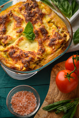 Ready Italian lasagna, on a green wooden background with basil, tomatoes. Culinary background, book of Italian recipes, delicious food. Vertical frame