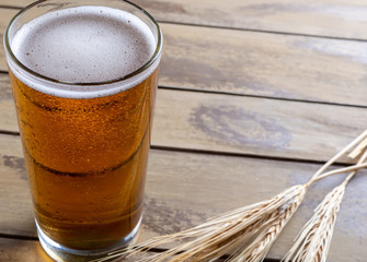 Glass of beer with ears of wheat on wooden background