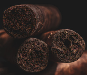 Three manly hand rolled havana cigars with shallow depth of field with dark backround.