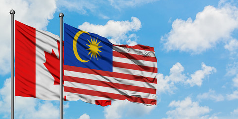 Canada and Malaysia flag waving in the wind against white cloudy blue sky together. Diplomacy concept, international relations.