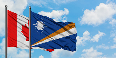 Canada and Marshall Islands flag waving in the wind against white cloudy blue sky together. Diplomacy concept, international relations.