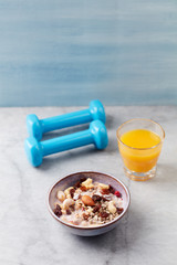 Bowl of granola with yogurt, nuts, raisins, cranberries and chia seeds. Blue dumbbells in background. Concept for a tasty and healthy meal. Stone - wooden background.Copy space.