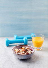 Bowl of granola with yogurt, nuts, raisins, cranberries and chia seeds. Blue dumbbells in background. Concept for a tasty and healthy meal. Stone - wooden background.Copy space.