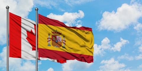 Canada and Spain flag waving in the wind against white cloudy blue sky together. Diplomacy concept, international relations.