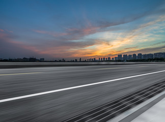 Asphalt road and the beautiful urban skyline at sunset
