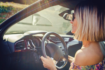 Woman driving a car wearing summer dress and sunglasses in a sunny autumn day entering or getting out of the car automobile