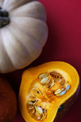 Orange and pale pumpkins with the seeds lying on the red background. Top view, flat lay