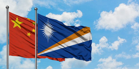 China and Marshall Islands flag waving in the wind against white cloudy blue sky together. Diplomacy concept, international relations.